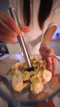 Woman from Asia smashing bananas with pestle in glass container for cooking