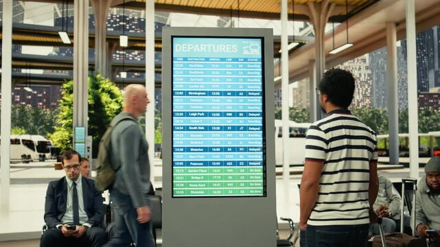 Black commuter gathers near information board in busy city bus station during rush hour, waiting for urban transport commercial services. People in a fast-paced public transportation hub.