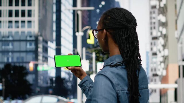 Isolated chroma key on smartphone near woman in the city center, relaxing by looking at social media posts on feed. African american girl using mockup device to browse internet, urban landscape.