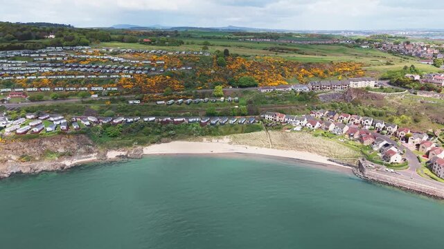Aerial cinematic drone backward reveal shot of Pettycur Bay sandy beach and holiday caravan park on the hillside, Fife, Scotland