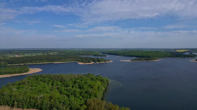 Aerial drone footage of Lake Narie near Morąg in the Warmia-Masuria region of northern Poland, featuring forested islands, tranquil bays and scenic landscape with blue water and natural shoreline
