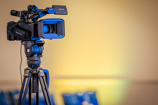 Riga, Latvia - May 15, 2026: Sony video camera mounted on tripod with blurred background of chairs in a conference setting, lighting creating a soft gradient effect