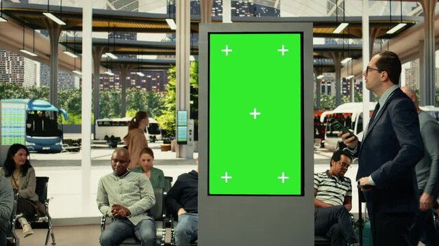 Chroma key screen in busy urban transit hub with diverse passengers waiting for city bus routes and shuttle services. People gather near schedule board during rush hour traffic.