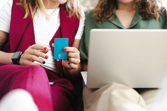 Two women are using a laptop and a credit card for online shopping or banking.
