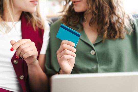 Two women are looking at a credit card and a laptop, suggesting online shopping or financial planning.