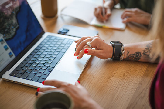 A woman's hands are shown working on a laptop, with another person writing in a notebook in the background, suggesting collaboration or study.