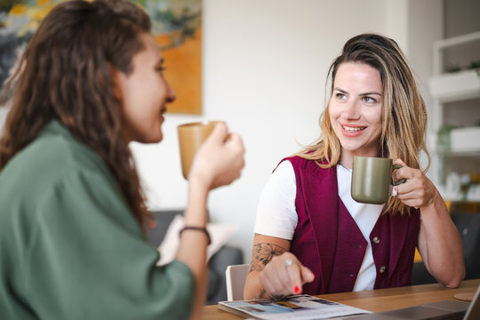 Two women are having a conversation over coffee at a table, discussing documents and a laptop.