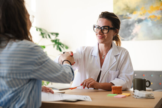 A doctor in a white coat shakes hands with a patient across a desk, signifying a successful consultation and positive outcome.