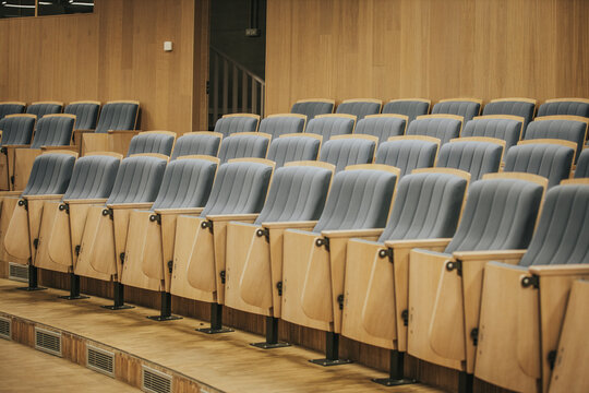 Rows of modern auditorium seats with blue upholstery and wooden armrests arranged in a spacious hall designed for presentations and lectures