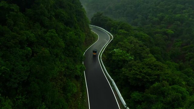 Aerial drone shot of a classic South Indian auto rickshaw driving along the winding mountain curves of Charmadi Ghat, Karnataka, India.