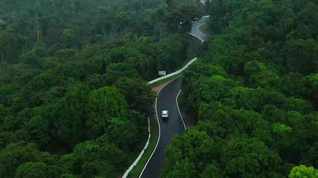 Birds-eye view of a white vehicle navigating sharp hairpin turns on a lush green mountain road, cinematic road trip concept.
