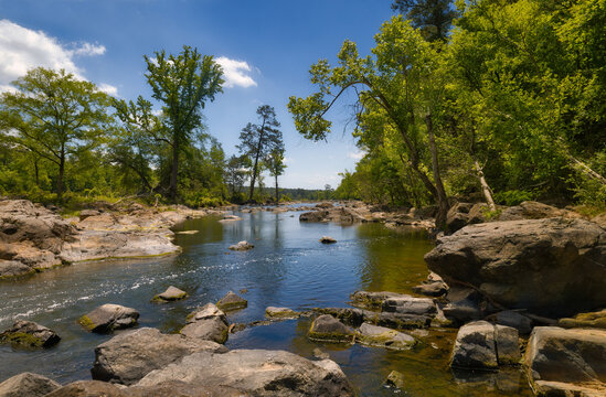A nice freshwater river under a cloudy blue sky with rocks and trees in the forest near beautiful Pittsboro, North Carolina in the United States.