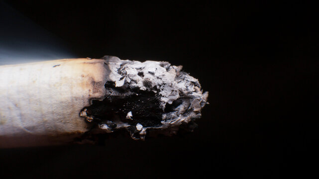 Close-up of a smoldering cigarette burning with ash falling