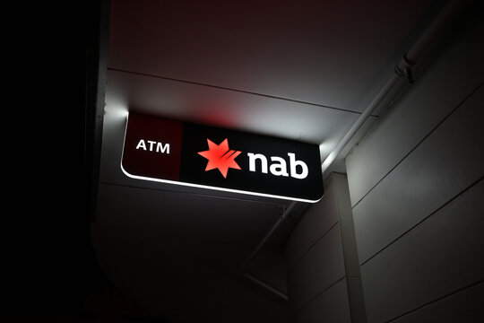 Illuminated NAB ATM sign, featuring the bank's red star logo, hanging outside of one of their branches at night