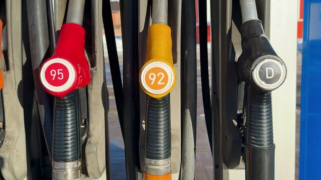 Closeup gas pump nozzles lined vertically, worn plastic handles with red yellow and black caps, coiled hoses and metal dispenser.