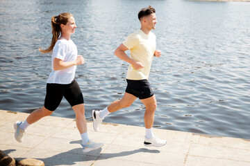 Fototapeta premium People jogging along a scenic riverside pathway during bright and sunny morning hours