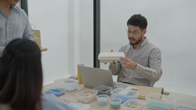 Office meeting team discussion with young man and woman, laptop on desk, prototype and presentation in business workspace, lunch delivery handoff and sample tray discussion in modern office room