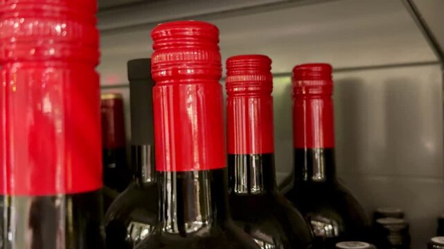 Close-up red wine bottle necks, rows of assorted brands on store shelf with glossy foil caps and visible cork tops, tight framing.