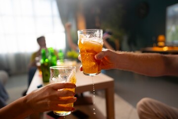 Fototapeta premium Two people raise their glasses to toast during a social gathering. The room has soft lighting, and friends are seen enjoying drinks together. Laughter fills the atmosphere.