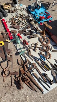 Vintage tools spread on blanket sunlit flea market display of rusty pliers wrenches horseshoes bolts and hand tools collector.