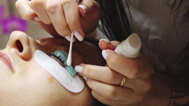 A young cosmetologist cleans eyelashes with a cotton swab.