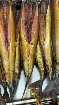 Cold smoked salmon balyk on counter, close-up of hanging golden fillets with visible salt crystals on metal rack inside fish shop.