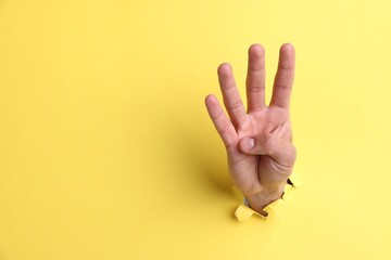 Naklejka premium Man showing number four with fingers through hole in yellow paper, closeup. Space for text