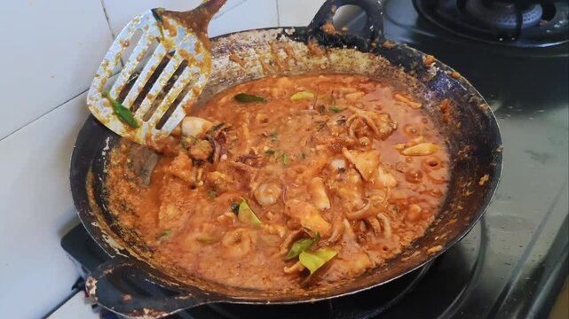 Indonesian spicy squid dish simmering in a red chili sauce, topped with fresh basil and lime leaves in a wok