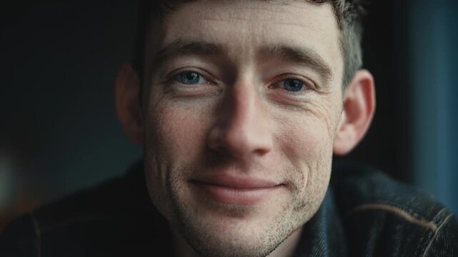 Handsome young man with warm subtle smile in moody indoor portrait
