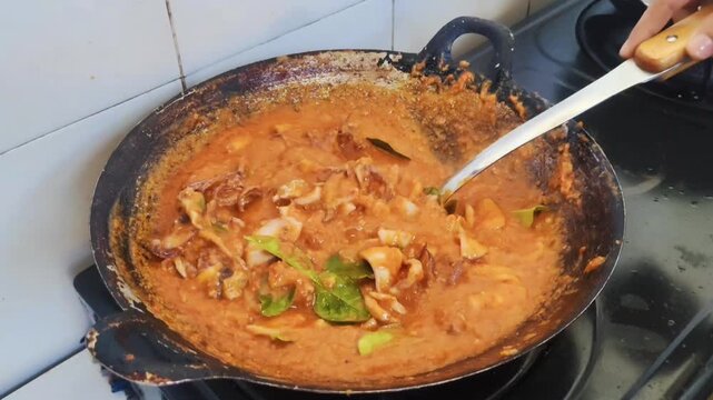 Indonesian spicy squid dish simmering in a red chili sauce, topped with fresh basil and lime leaves in a wok