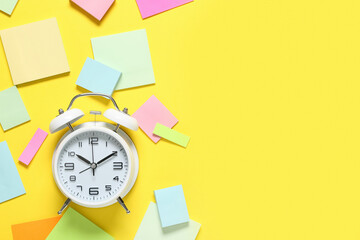 Fototapeta premium Alarm clock with sticky notes on yellow background. Time management concept