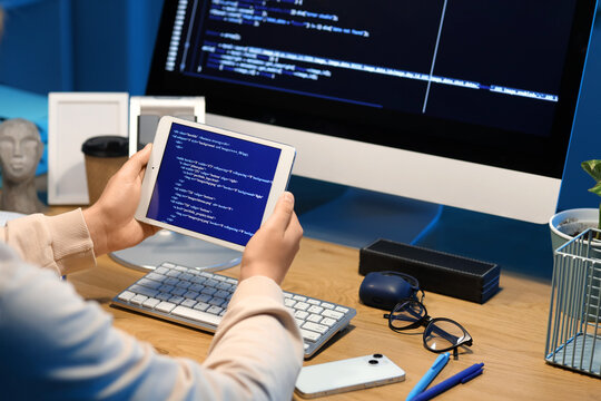 Female programmer working with modern tablet computer at table in office, closeup