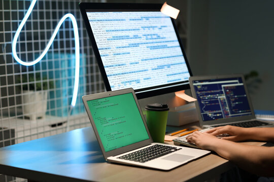 Male programmer working with computer keyboard and modern laptops at table in office, closeup