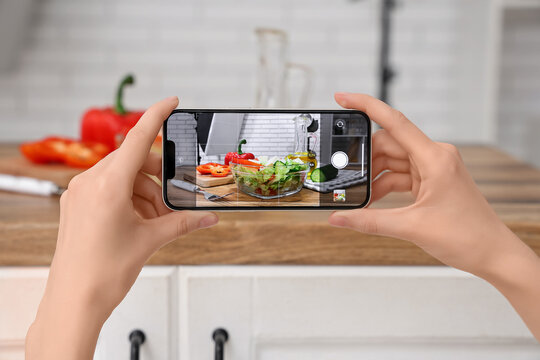 Female photographer with mobile phone taking picture of vegetable salad on table in studio, closeup
