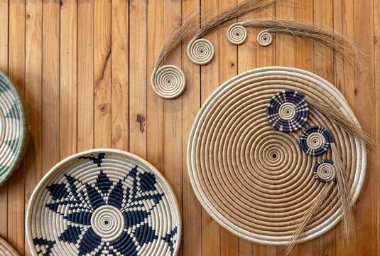 Traditional handwoven Rwandan wall baskets and raw sweetgrass fibers displayed on a wooden panel background in Kigali, Rwanda