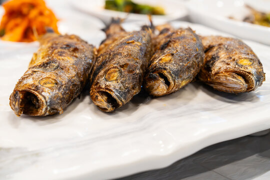 Side angle shot of four grilled whole yellow croakers on white platter