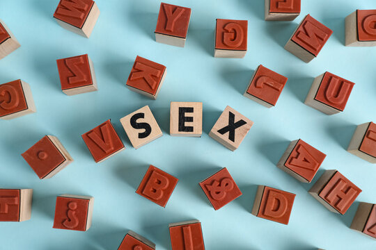 Word SEX made of wooden cubes on blue background
