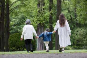 Fototapeta premium 春の新緑の公園で遊ぶおばあちゃんとお母さんと手を繋ぐ歩く寄り添う全身の後ろ姿顔無し 
