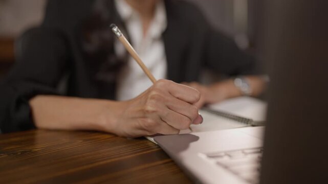 Hand writing in notebook on office desk with pencil, woman business work planning note paper on wooden table, close up blurred background creative project document stationery