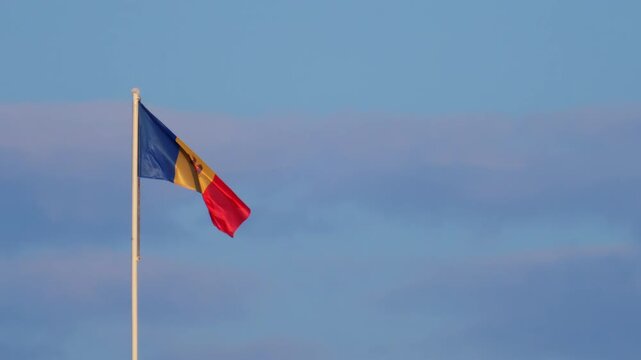 Moldovan national flag waving on a tall flagpole against a clear blue sky