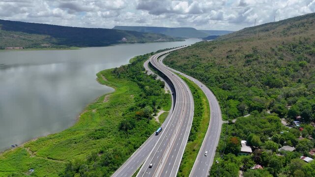 Aerial view of highway running along river and green hills. Transportation, infrastructure, travel and logistics concept