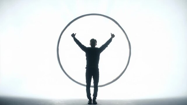 Silhouette of performer raising arms triumphantly inside spinning cyr wheel stage