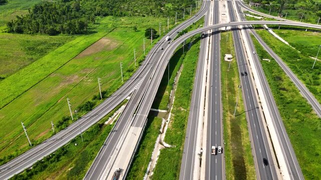 Aerial view of modern highway interchange with multilayer roads and curved ramps surrounded by green farmland, showcasing transportation infrastructure, urban development, and road network planning.