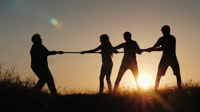 Silhouette of family playing tug of war game during sunset on grass field in park.