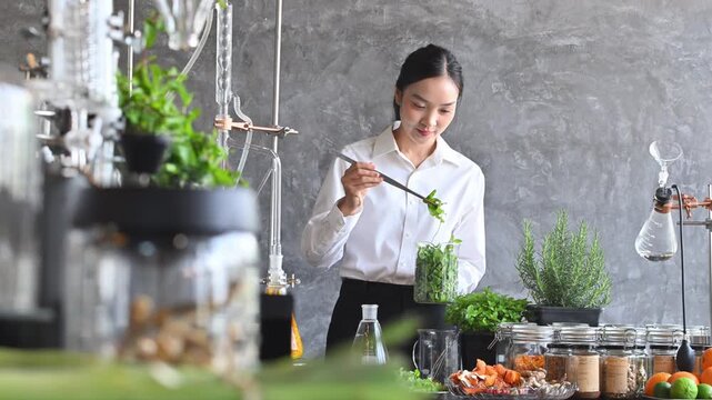 Young Asian Woman Scientist Formulating Natural Herbal Extract in Modern Laboratory with Fresh Botanicals and Distillation Equipment