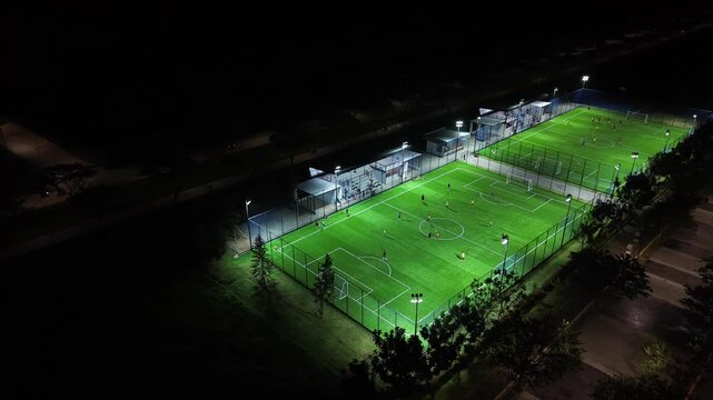 Aerial Drone View of Night Football Field with Players Training on Illuminated Artificial Turf