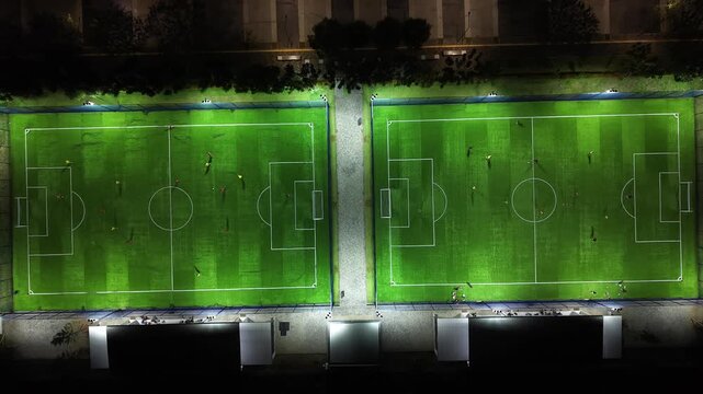Aerial Drone View of Night Football Field with Players Training on Illuminated Artificial Turf