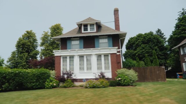 Driving through suburban neighborhood with brick houses and green trees.