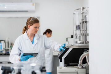 Naklejka premium Female scientist with tablet operating high tech equipment in laboratory, clinical research specialist working on scientific experiment, medical biotechnology analysis, pharmaceutical development.