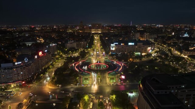 Aerial view of bucarest city at night with illuminated fountains and bustling traffic, showcasing vibrant urban movement.